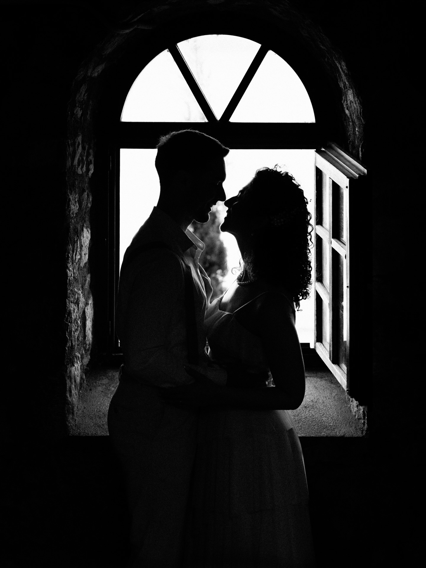 Newlyweds in silhouette beside a bright arched window